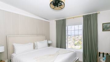 A hotel room with a large bed, a window with curtains, a bedside lamp, and a view of the cityscape.