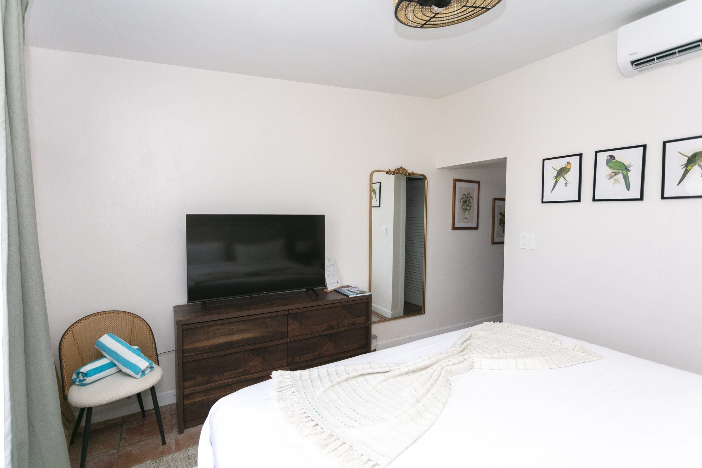 A bedroom with a bed, a TV, a dresser, a chair, and a mirror.