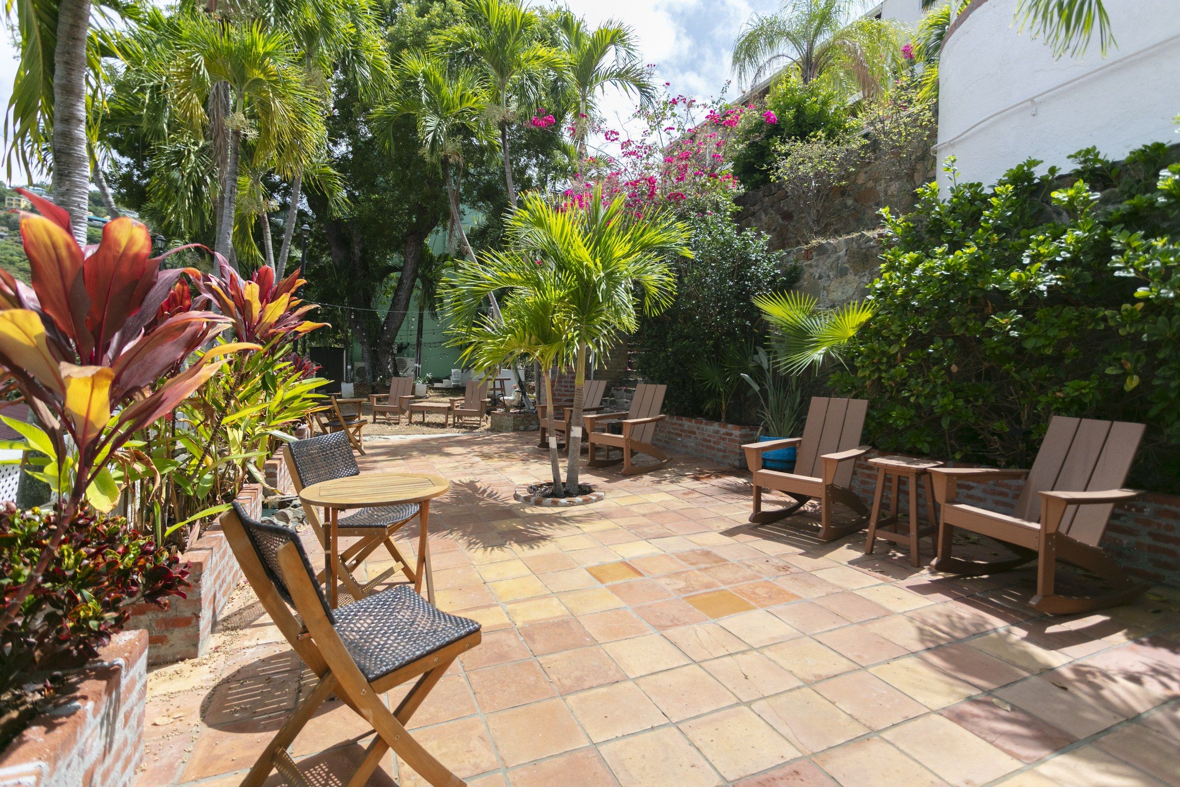 An outdoor patio with a tiled floor, wooden furniture, and various tropical plants.