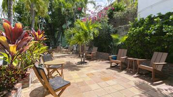 An outdoor patio with a tiled floor, wooden furniture, and various tropical plants.
