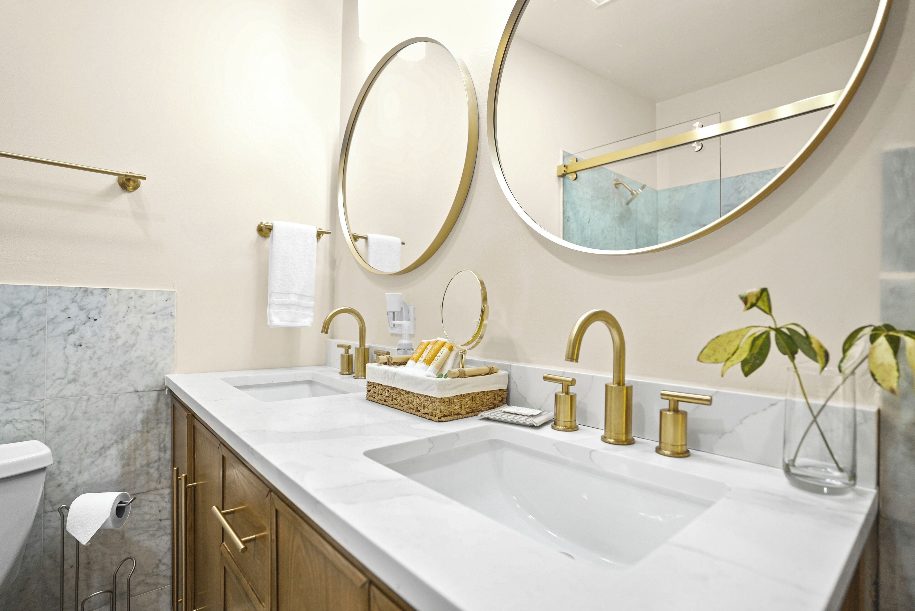 Une salle de bain moderne avec deux vasques, des robinets dorés et des plans de toilette en marbre.