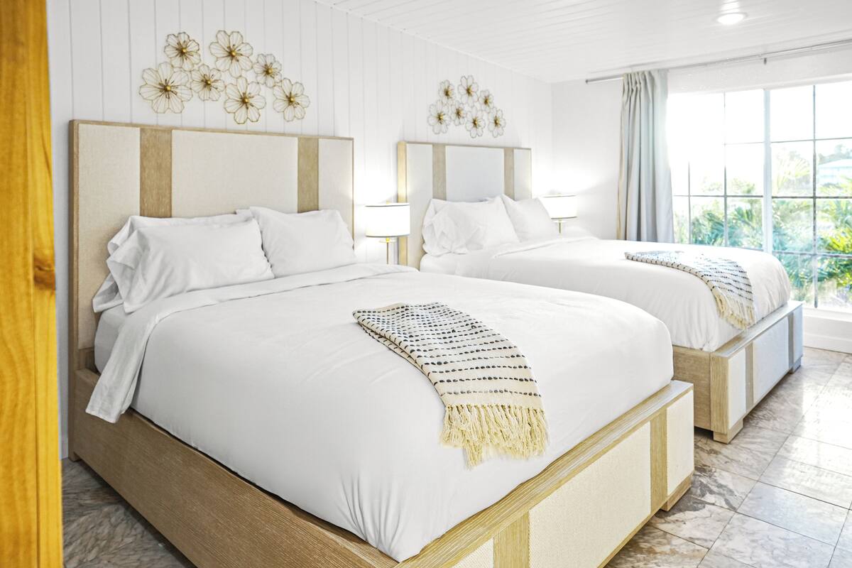 A hotel room with two beds, each with a wooden headboard, white bedding, and a decorative wall hanging.
