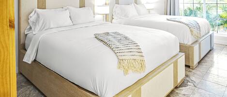 A hotel room with two beds, each with a wooden headboard, white bedding, and a decorative wall hanging.
