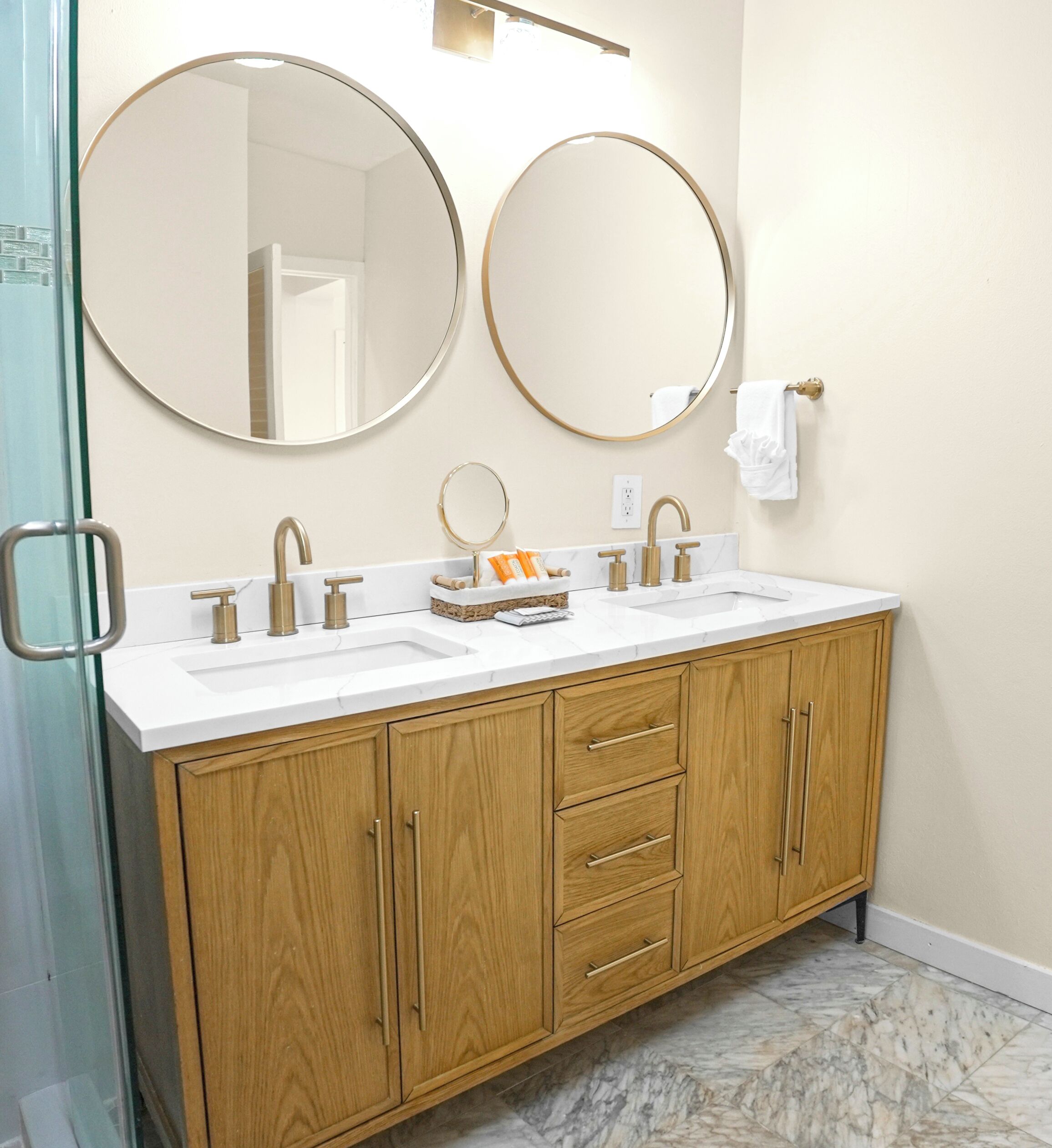 A bathroom with two sinks, wooden cabinets, and two round mirrors.