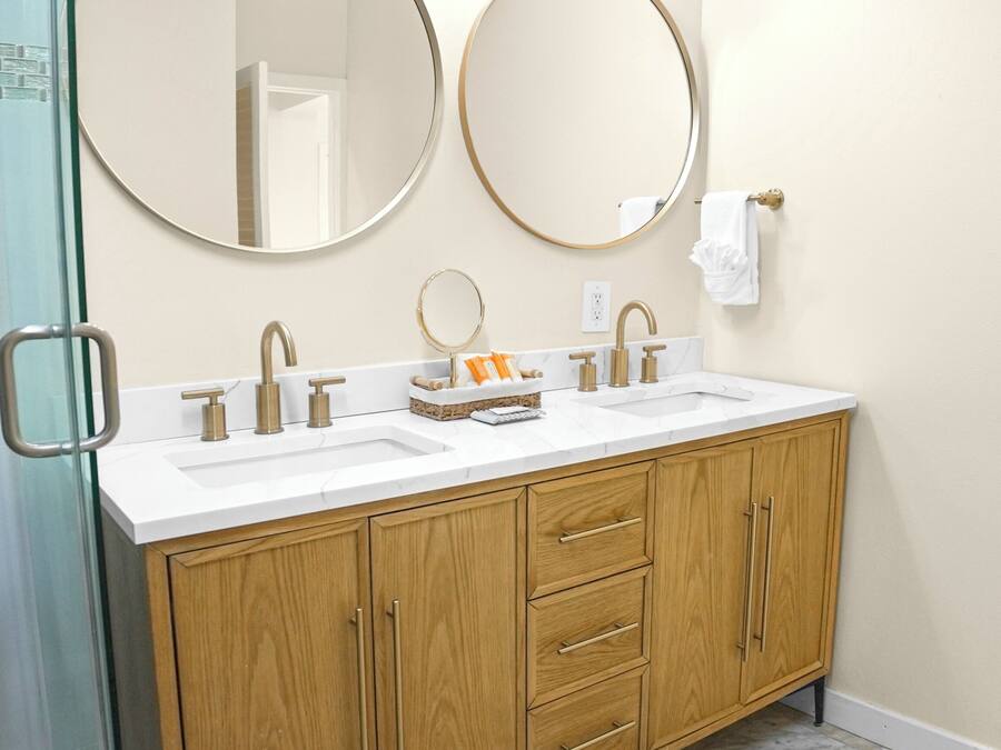 A bathroom with two sinks, wooden cabinets, and two round mirrors.