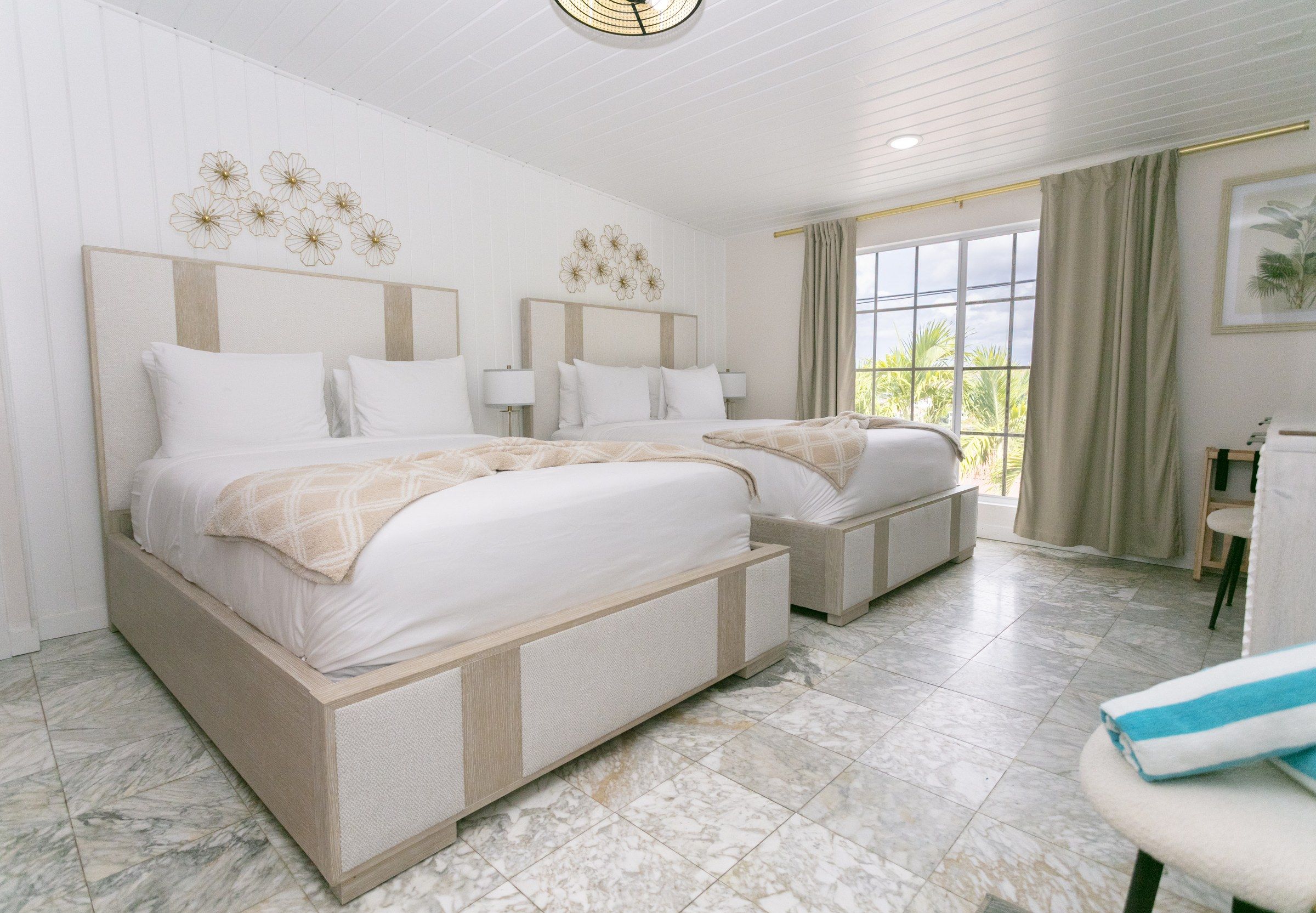 A hotel room with two beds, a large window, and a view of greenery outside.