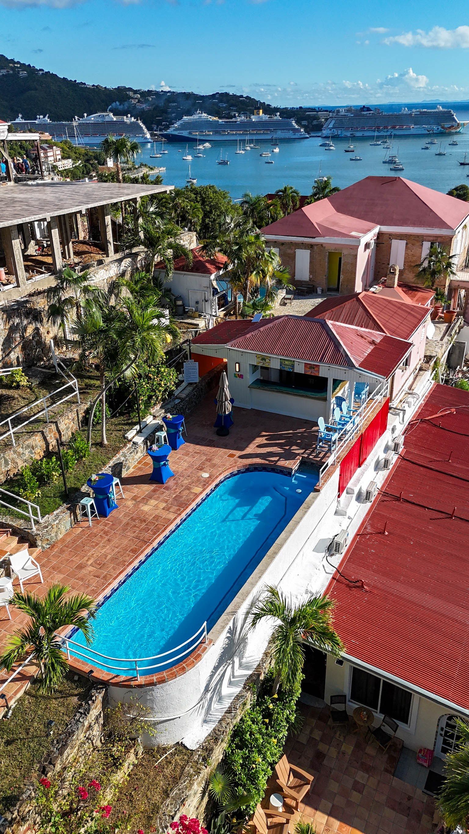 A residential area with a swimming pool, a red-roofed building, and a view of the sea with boats.