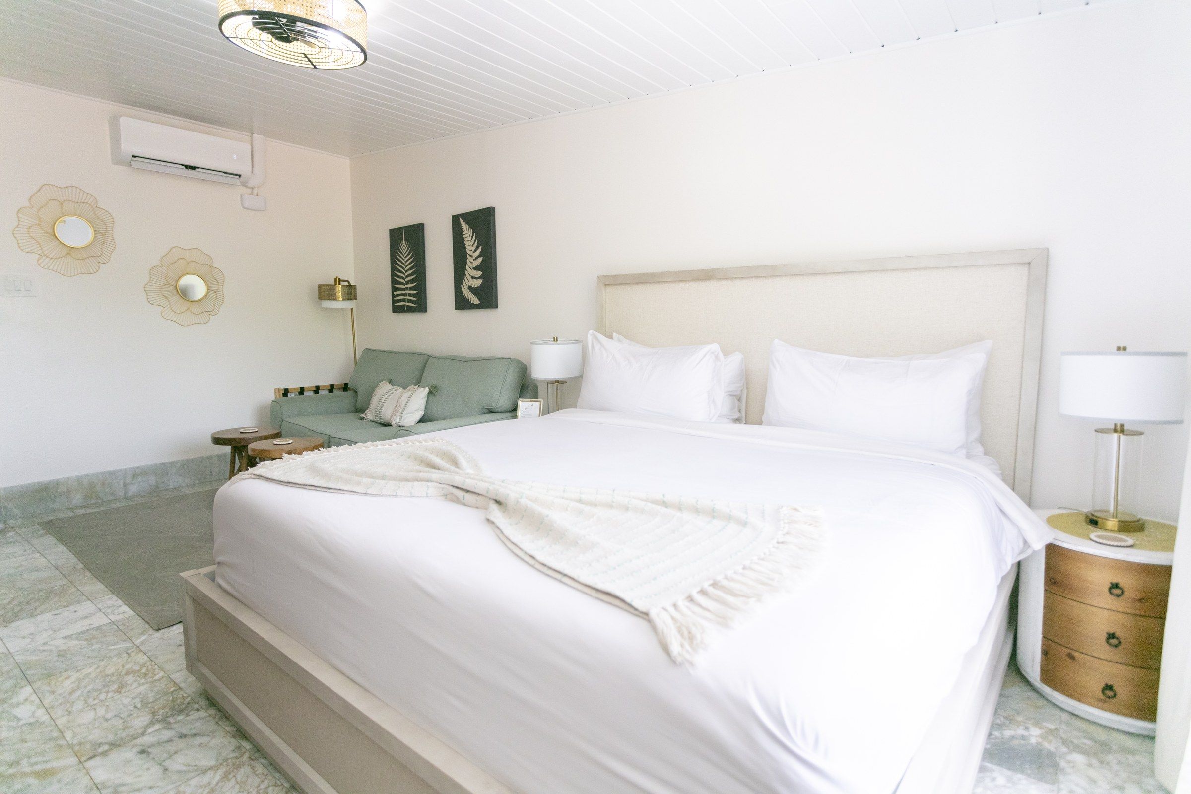 A hotel room with a large bed, a nightstand, a lamp, a wall-mounted air conditioner, and decorative wall art.