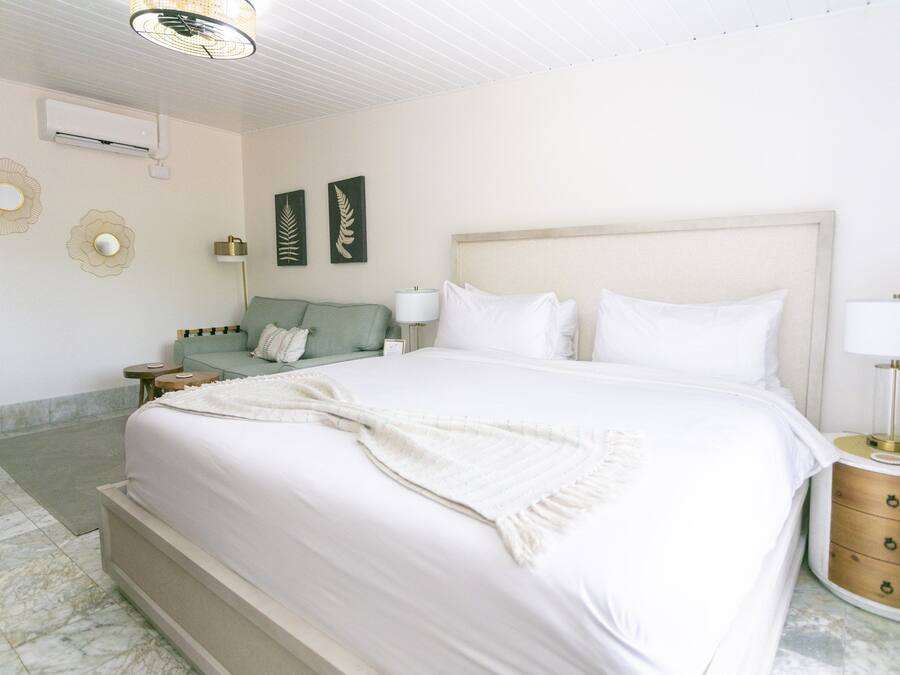 A hotel room with a large bed, a nightstand, a lamp, a wall-mounted air conditioner, and decorative wall art.