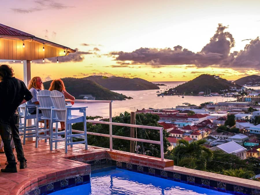 A poolside area with chairs and a view of a coastal town at sunset.