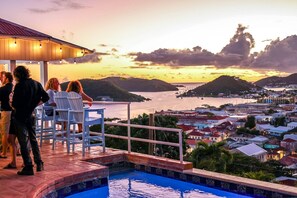 Un espace aménagé au bord de la piscine, avec des chaises et une vue sur une ville côtière au coucher du soleil.