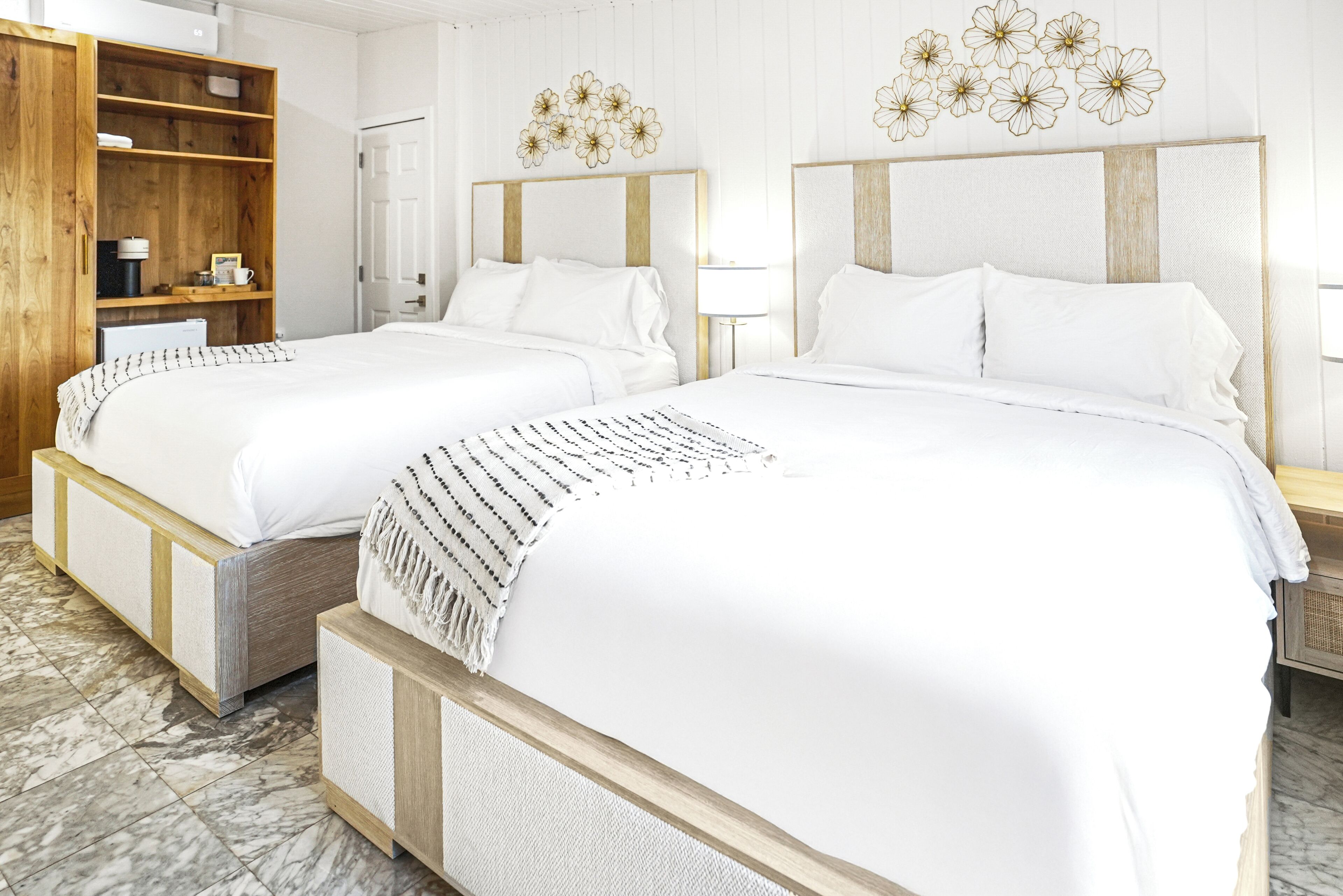 A hotel room with two beds, wooden headboards, a wooden wardrobe, and a marble floor.
