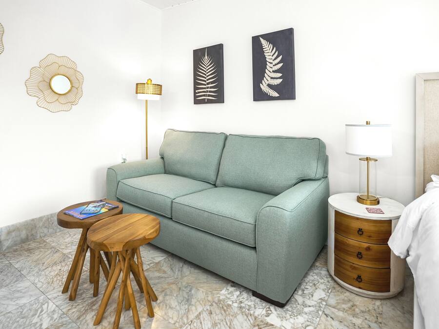 A modern room with a teal sofa, a wooden side table, a lamp, and a bedside table with drawers.