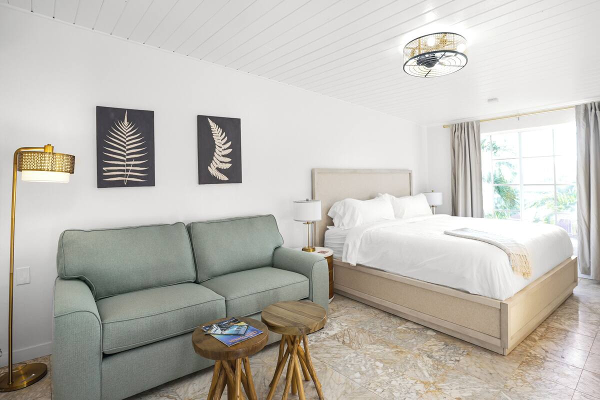 A hotel room with a bed, a sofa, a small wooden table, and a floor lamp.