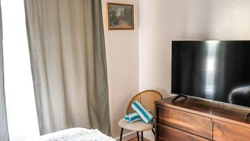 Une chambre d’hôtel avec un lit, une commode en bois, une télévision, une chaise et un tableau accroché au mur.