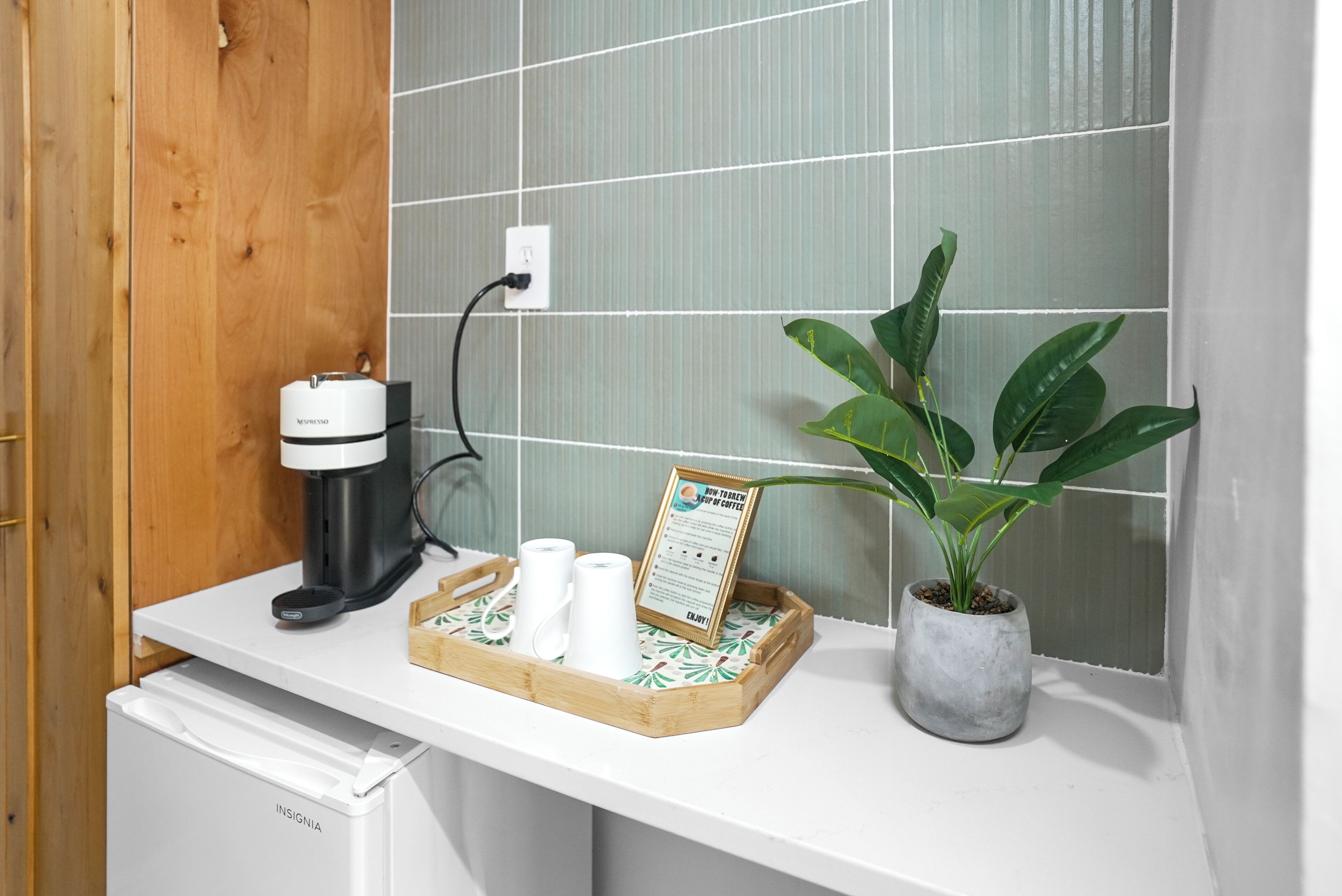 Una encimera de cocina con una cafetera, una bandeja con tazas de café, un cartel y una planta en maceta.