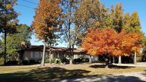 Une maison à deux étages avec un jardin devant, entourée d’arbres aux feuilles d’automne.