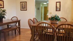 Un coin repas avec une table et des chaises en bois, des tableaux encadrés aux murs et une plante en pot sur la table.