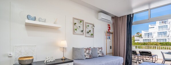 Ein modernes Hotelzimmer mit einem Bett, einem Schreibtisch, einer Lampe, Dekoration und Blick auf die Stadt durch große Fenster.