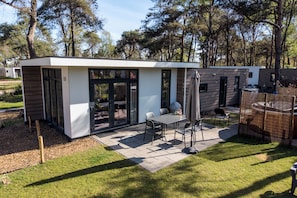 Un patio exterior moderno con mesa y sillas, un espacio de estar cubierto y una zona de juegos cercada.
