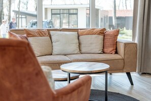 Un salon moderne avec un canapé beige, une table basse ronde en bois et une grande fenêtre donnant sur un quartier résidentiel.