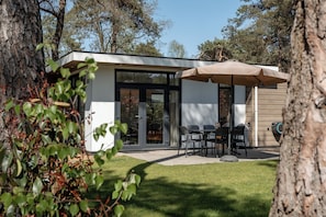 Una casa moderna con un patio, mobiliario exterior y una zona cubierta.