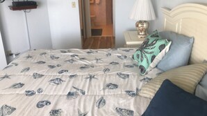 A bedroom with a bed, a TV mounted on the wall, a bedside lamp, and a door leading to a bathroom. - Oceanfront Sand Dollar Condo 601 (Daytona Beach Shores)