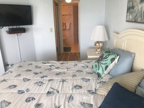 A bedroom with a bed, a TV mounted on the wall, a bedside lamp, and a door leading to a bathroom.