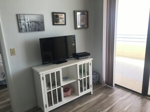 A living room with a flat-screen TV on a white cabinet, a small shelf, and three framed pictures on the wall.
