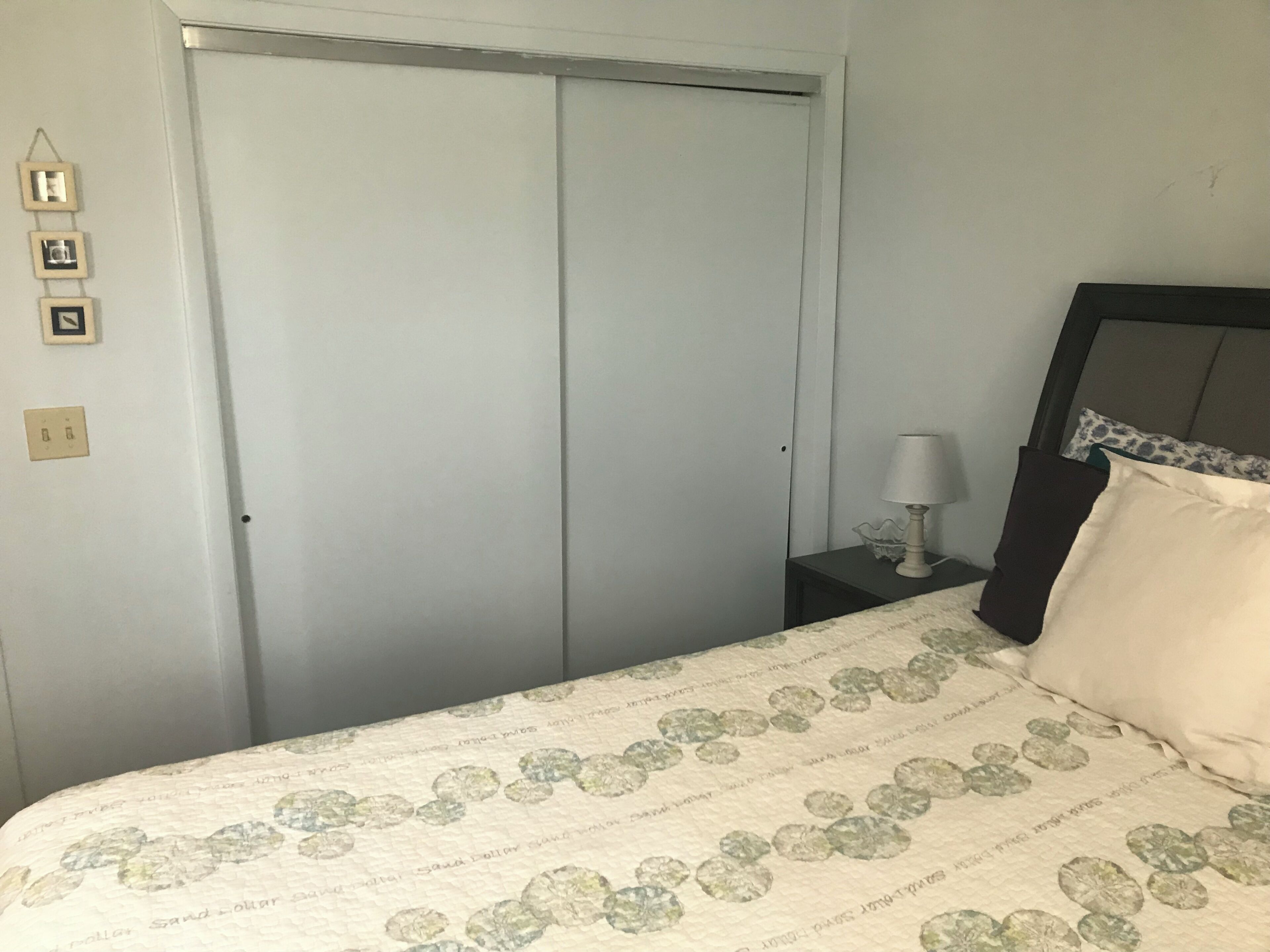 A bedroom with a bed, a nightstand, a lamp, a bedside table, and a wardrobe.