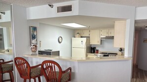 A compact kitchen with a central island, wooden chairs, and a refrigerator. - Oceanfront Sand Dollar Condo 601 (Daytona Beach Shores)
