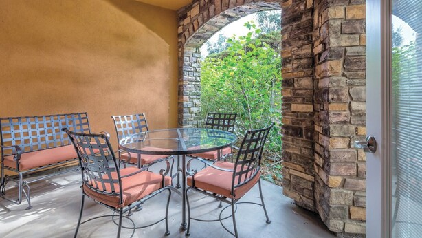 Une terrasse dotée d’une table en verre et de chaises en métal, entourée de murs en pierre et offrant une vue sur la verdure.