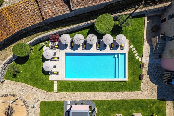 An aerial view of a swimming pool with a stone deck, surrounded by lounge chairs and umbrellas, and bordered by a stone wall and greenery. - Casa Da Brêa Viana do Castelo (Viana do Castelo)