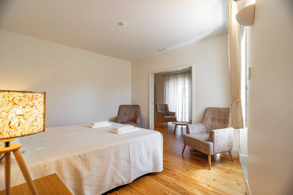 Une chambre d’hôtel avec un grand lit, deux fauteuils, une petite table et une lampe.