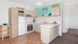 A modern kitchen with white cabinetry, a built-in microwave, a stove, and a sink. - Coastal Vibes with a touch of convenience (Rockingham)