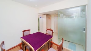 A room with a wooden table, purple tablecloth, and chairs. There is a glass partition and a door leading to another room.