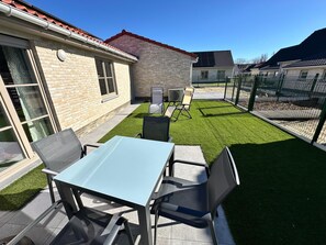 Een terras met een tafel en stoelen, een klein gazon en een gebouw met een bakstenen gevel.