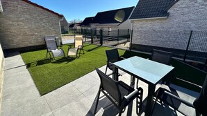 Un patio con mesa y sillas, un pequeño césped y un muro de ladrillo.