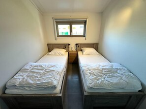 Een kleine, schone kamer met twee eenpersoonsbedden, een raam en een houten hoofdbord.