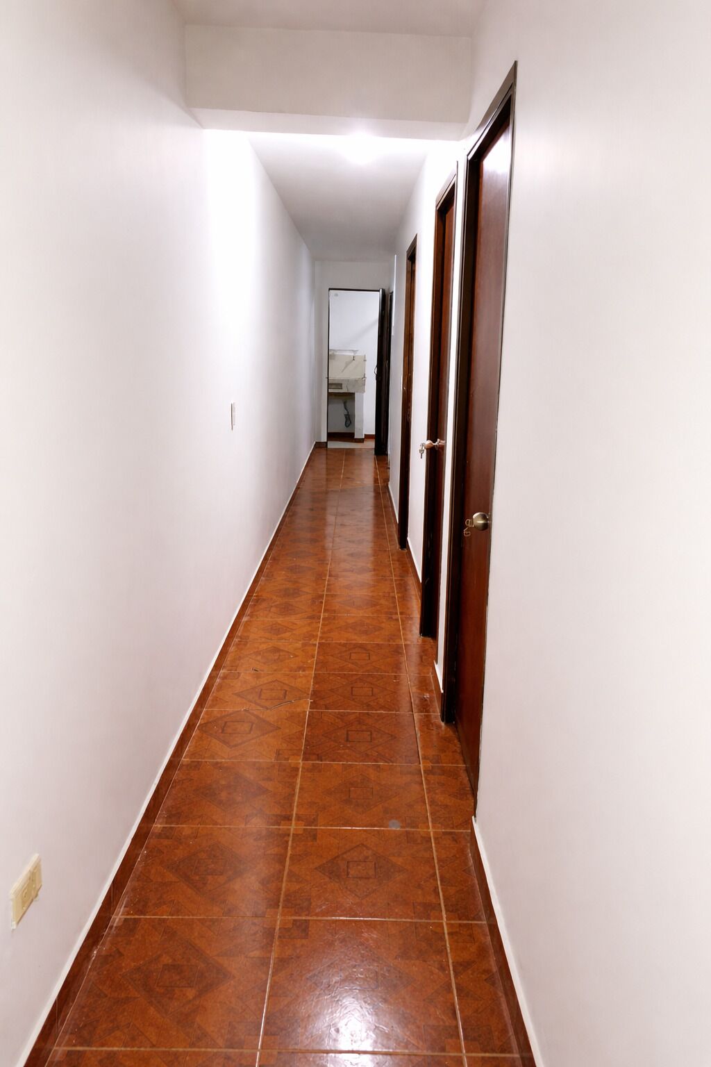 A long, narrow hallway with a tiled floor and wooden doors on one side.