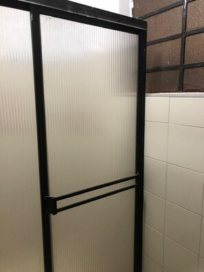 A bathroom with a frosted glass partition, white tiled walls, and a black metal frame.
