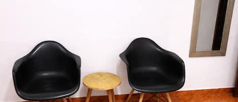 Dos sillas negras y una pequeña mesa redonda en una habitación con suelo de madera y un espejo en la pared.