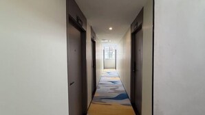 Un long couloir étroit, avec des portes de chaque côté, qui mène à une pièce lumineuse au bout.