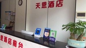 Un comptoir d’accueil d’hôtel avec une horloge, une enseigne indiquant « 天恩酒店 » et une plante en pot.