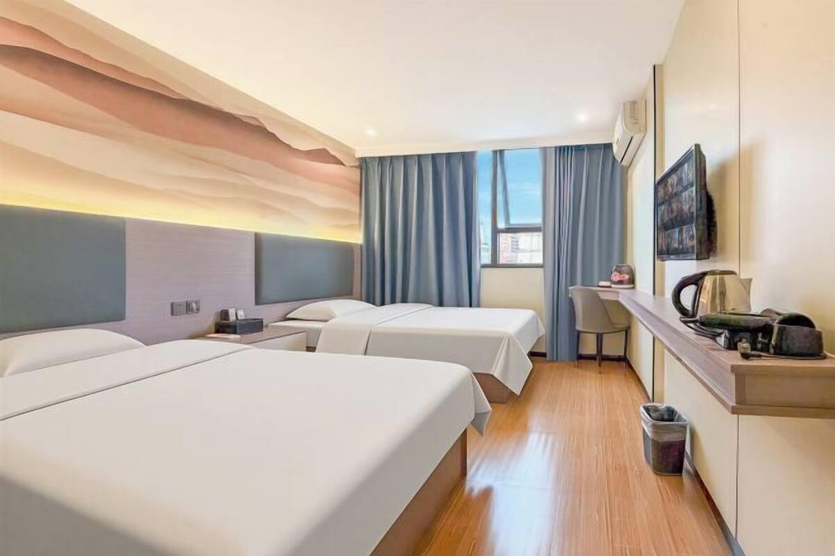 A hotel room with two beds, a desk, a chair, a TV, and a window with curtains.