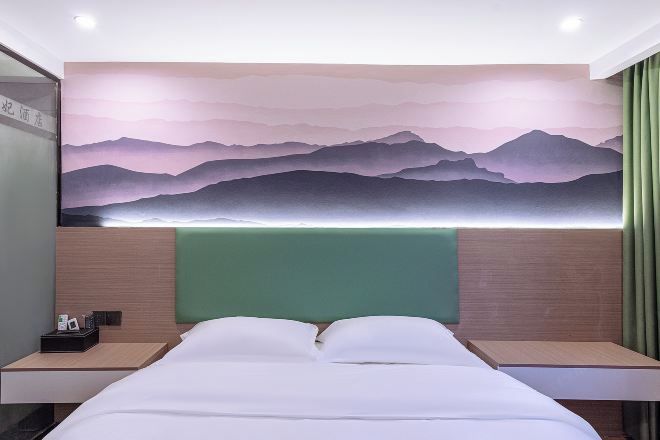 A hotel room with a bed, two bedside tables, a green headboard, and a wall mural of mountains.