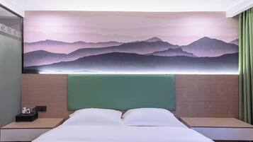 A hotel room with a bed, two bedside tables, a green headboard, and a wall mural of mountains.