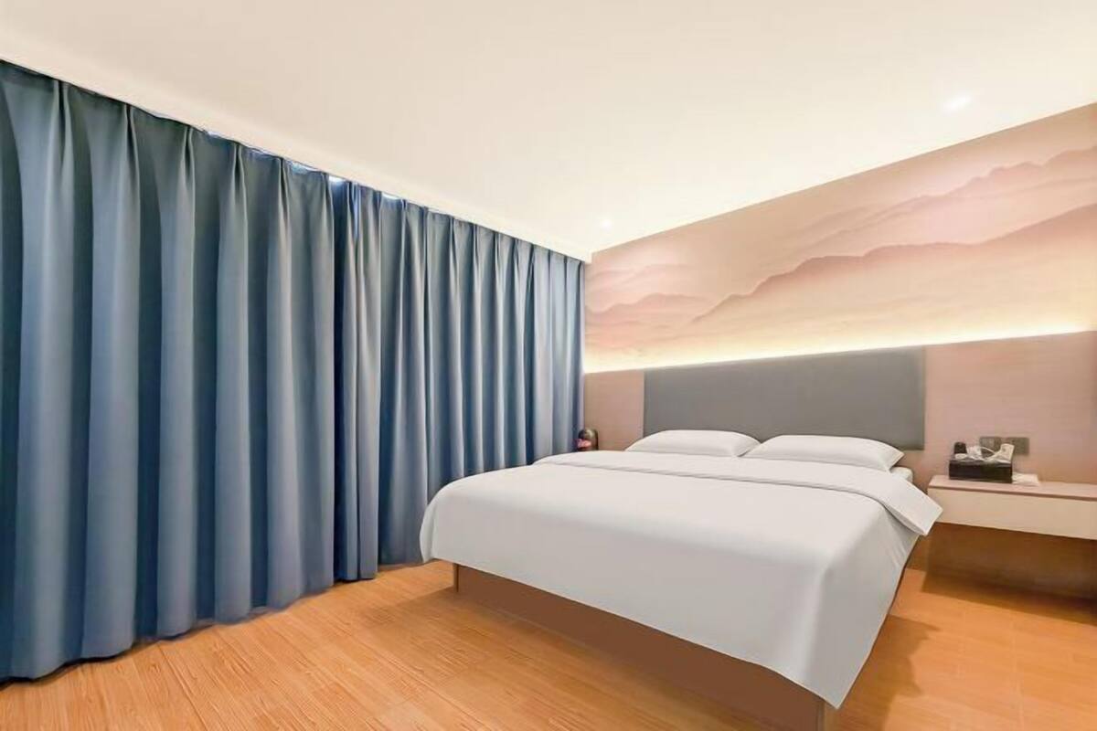 A modern hotel room with a bed, curtains, a nightstand, and a wall with a textured design.