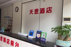 A hotel reception desk with a clock, a potted plant, and informational brochures. - Nanning Tian'en Hotel (Xiuxiang Metro Station, Guangxi University Branch) (Nanning)
