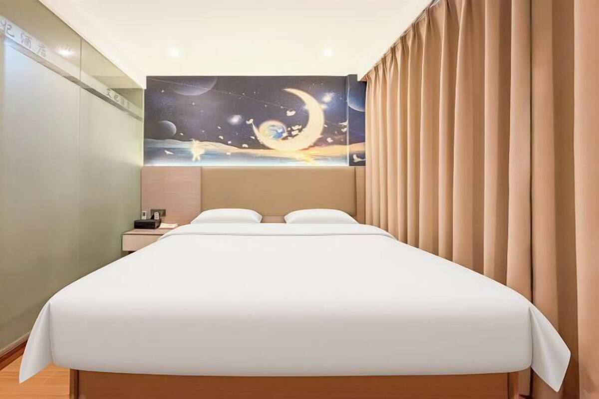 A hotel room with a bed, a night sky mural, a nightstand, and a window with curtains.